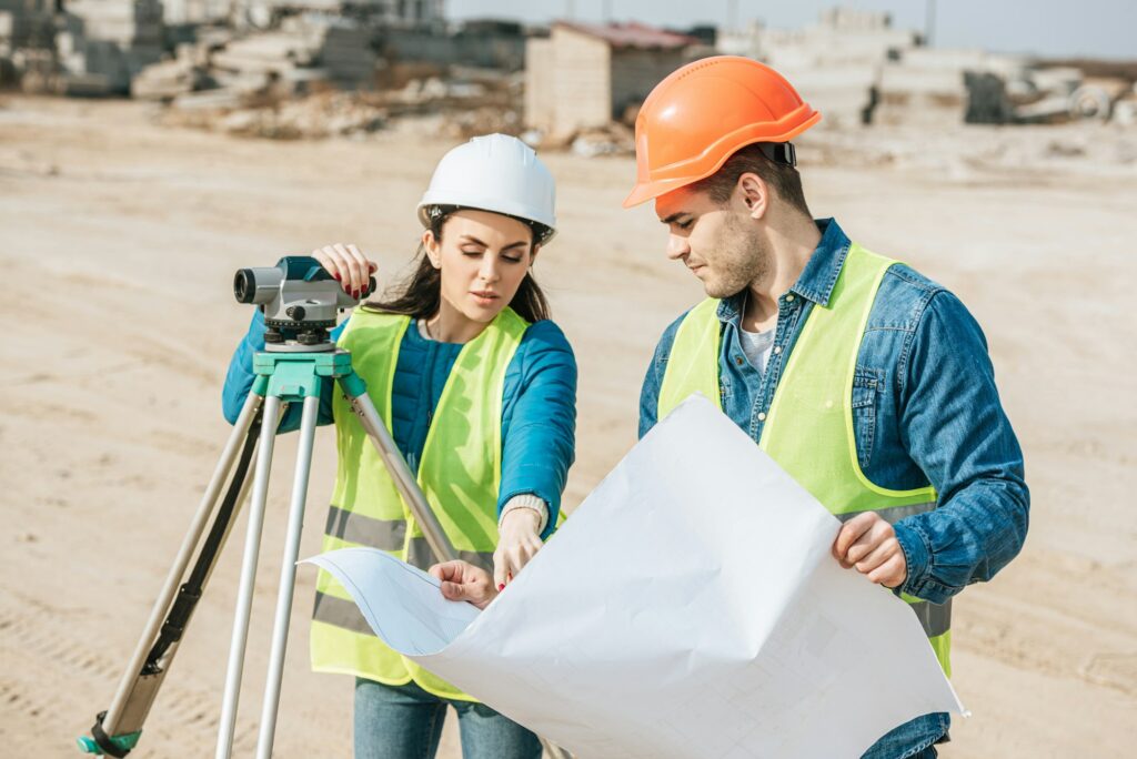 Surveyor with digital level pointing on blueprint to colleague